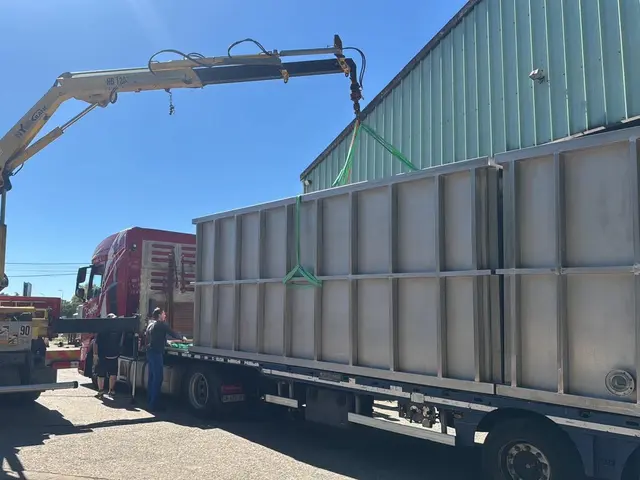 Grue auxiliaire chargeant une grande structure métallique sur une semi-remorque