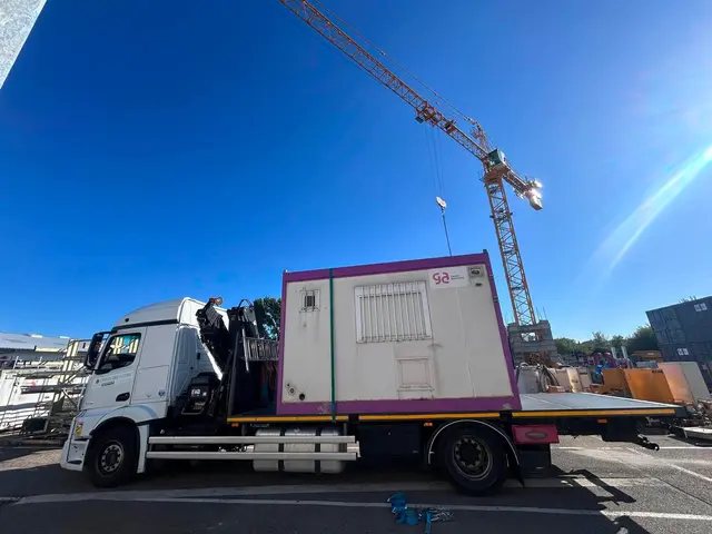 Camion-grue chargé d’un module préfabriqué sur un site équipé d’une grue à tour