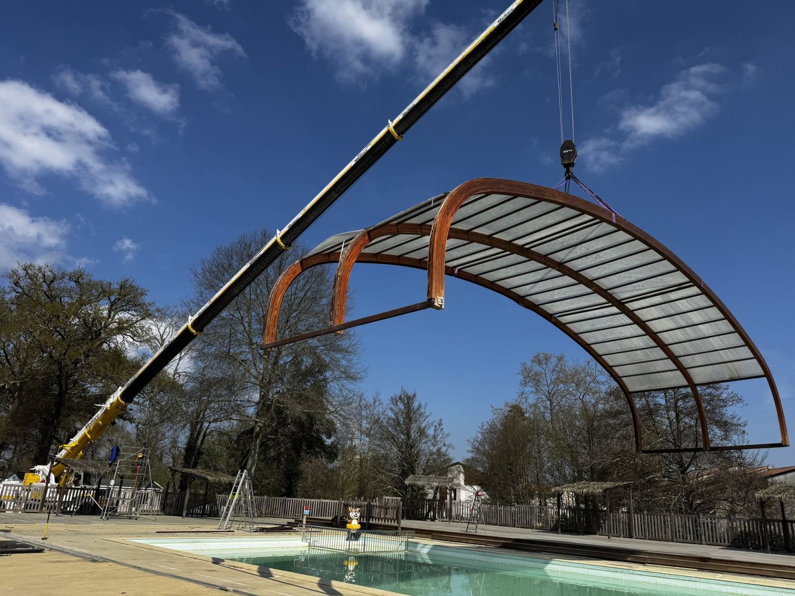 Une travée cintrée est levée par une grue au-dessus de la piscine.