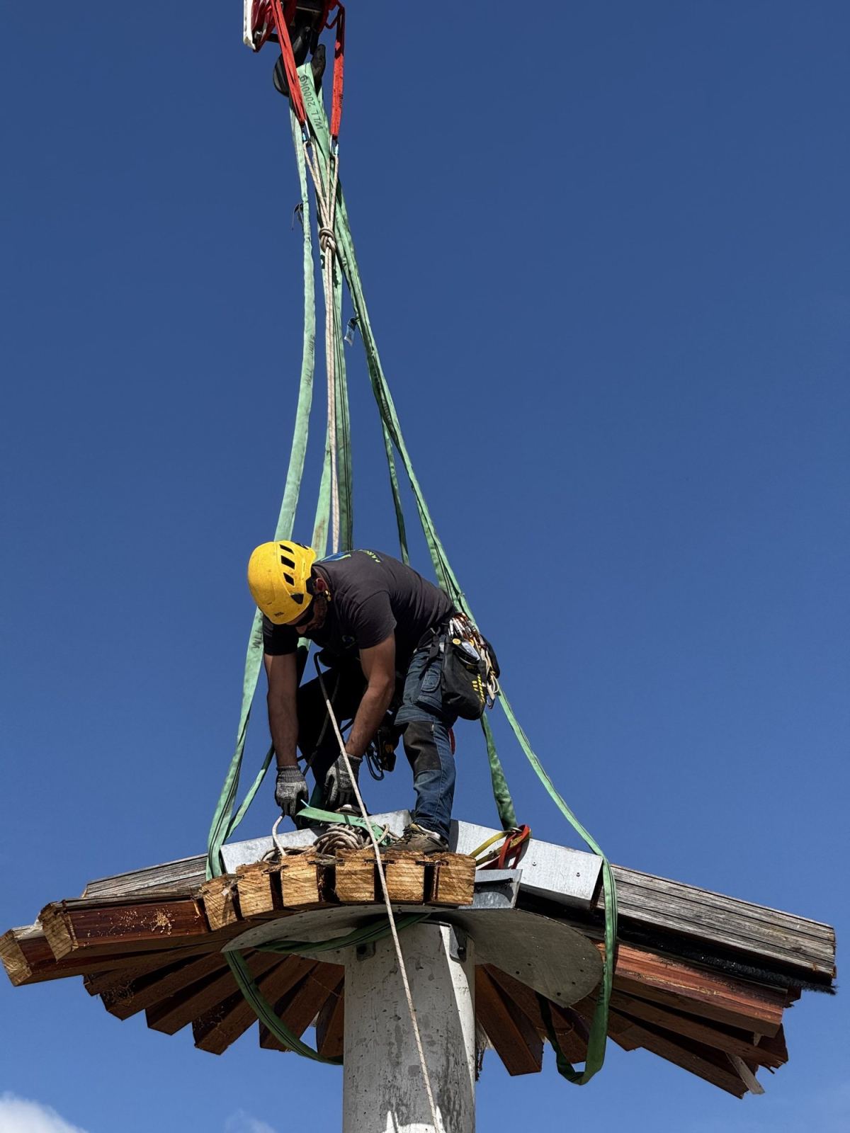 Technicien casqué fixe les élingues sur un élément en hauteur.