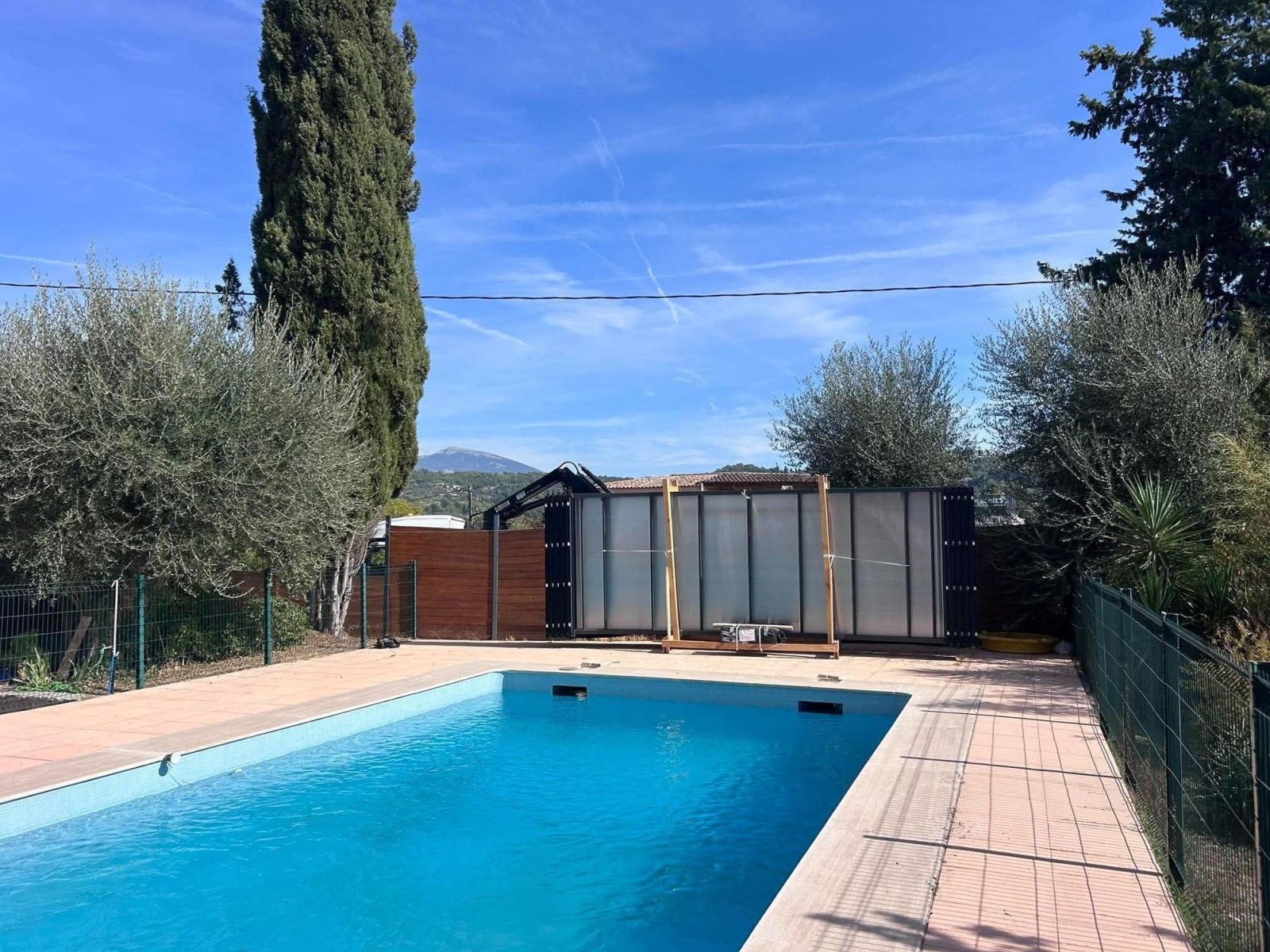 Éléments d’un abri de piscine regroupés au bord d’un bassin dans un jardin.