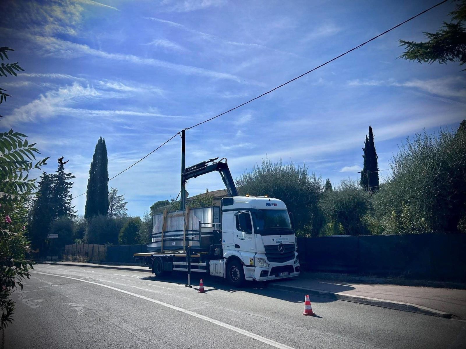 Camion-grue au bord de la rue pour charger un abri situé derrière une clôture.