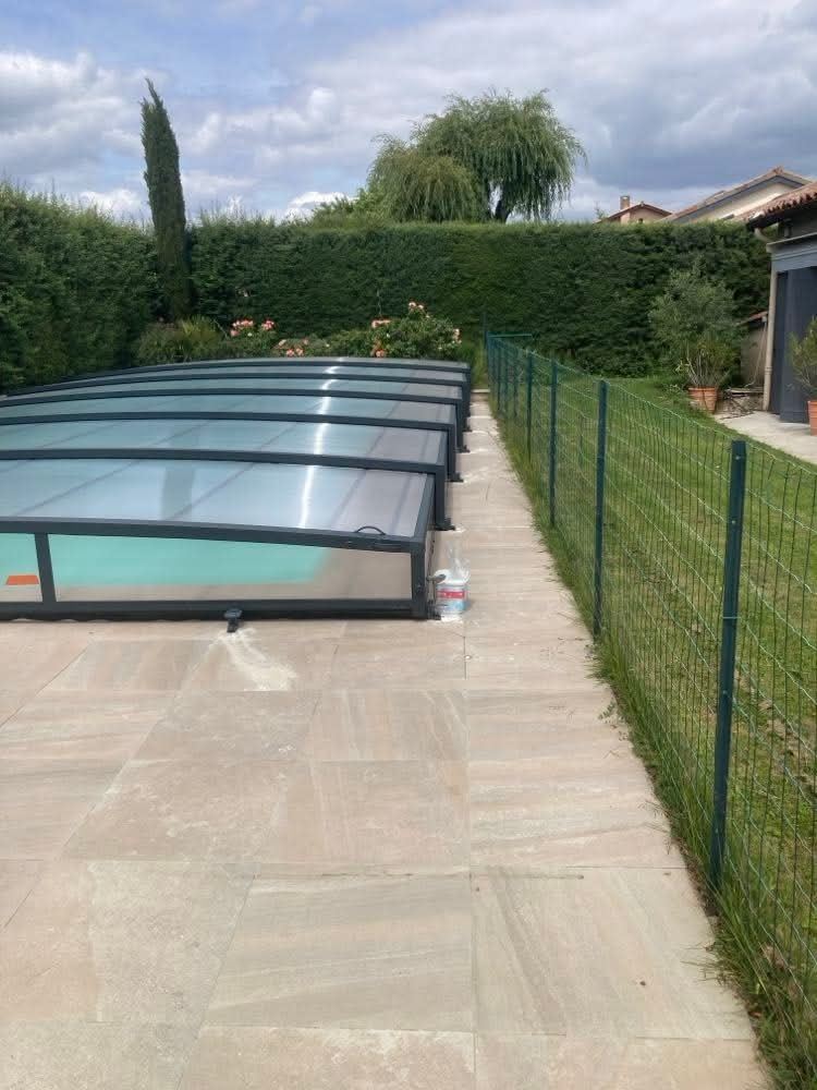 Abri bas télescopique transparent sur une piscine, à côté d’une pelouse et d’une terrasse.