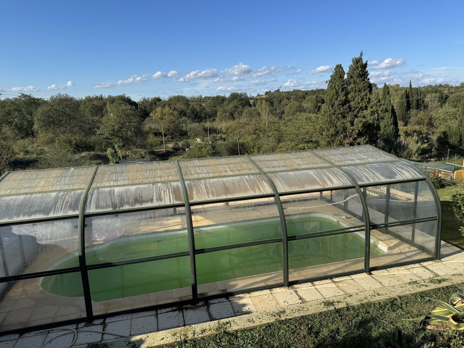 Abri de piscine cintré et télescopique installé dans un jardin.
