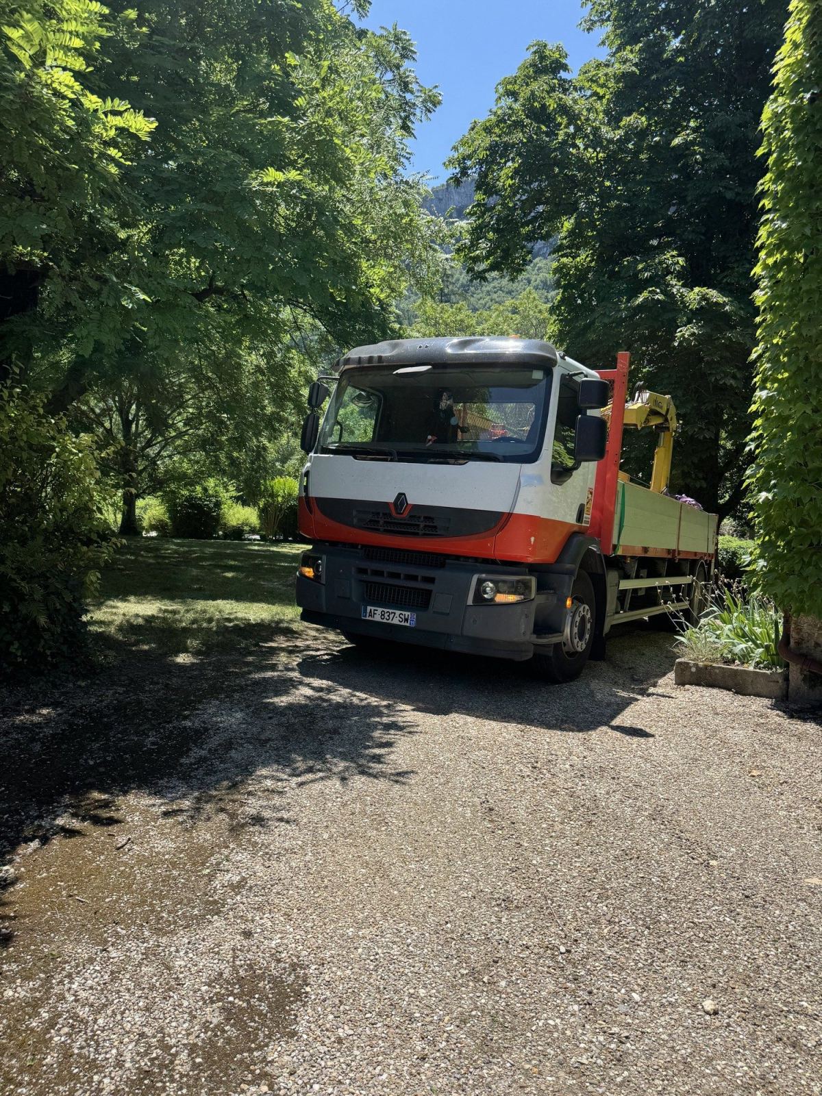 Camion-grue positionné sur une voie arborée menant à une propriété.