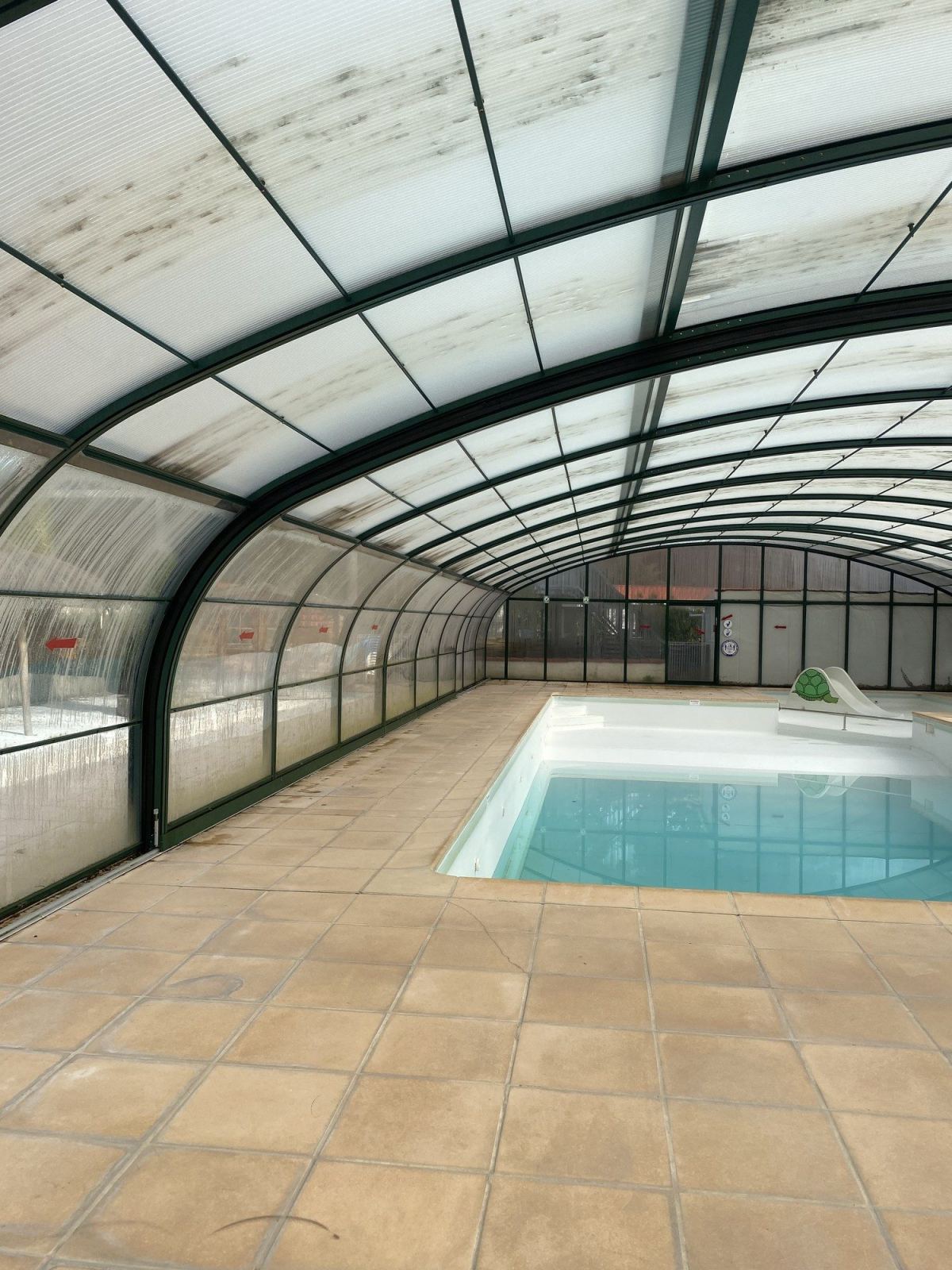 Bassin et terrasse sous un grand abri de piscine collectif.