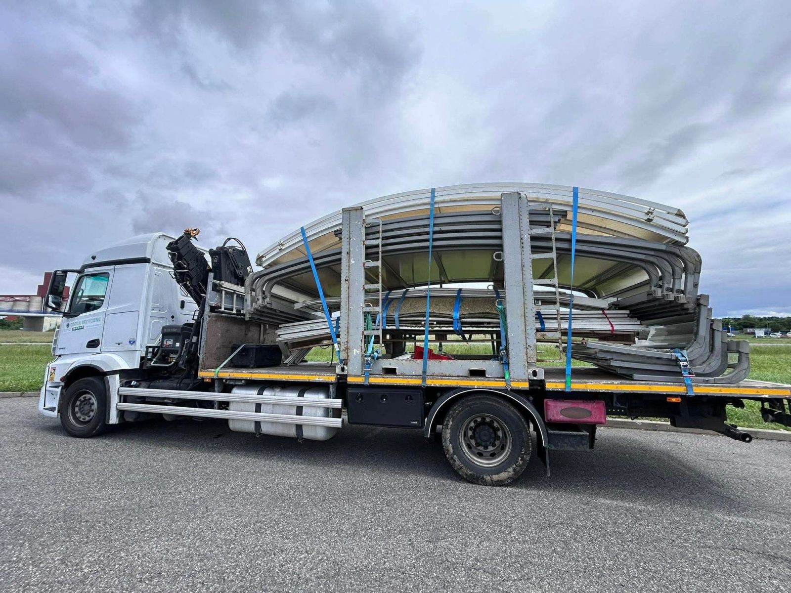 Éléments cintrés d’un abri de piscine empilés et arrimés sur un camion-grue.