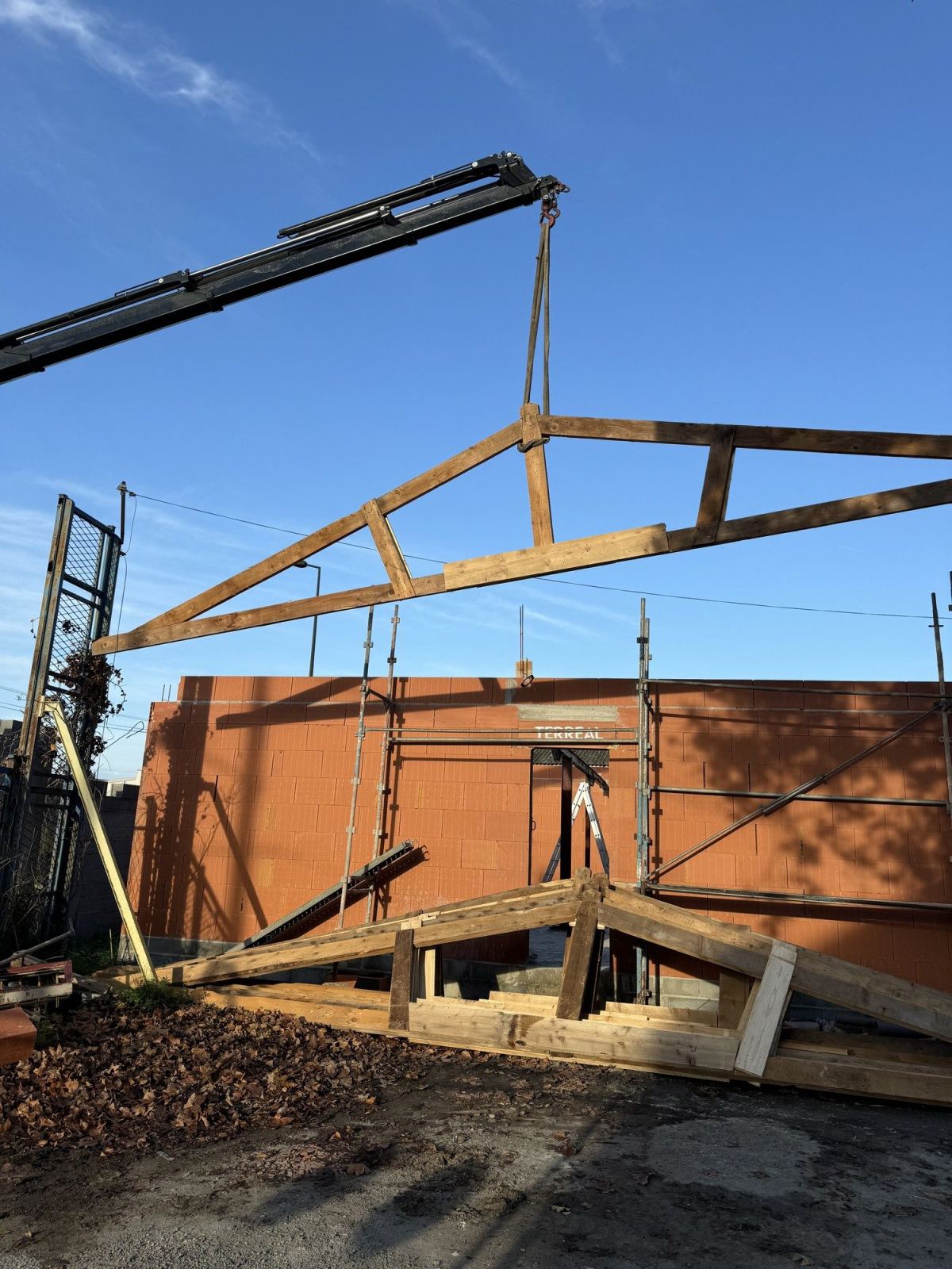 Une grue soulève une pièce de charpente en bois au-dessus du chantier.
