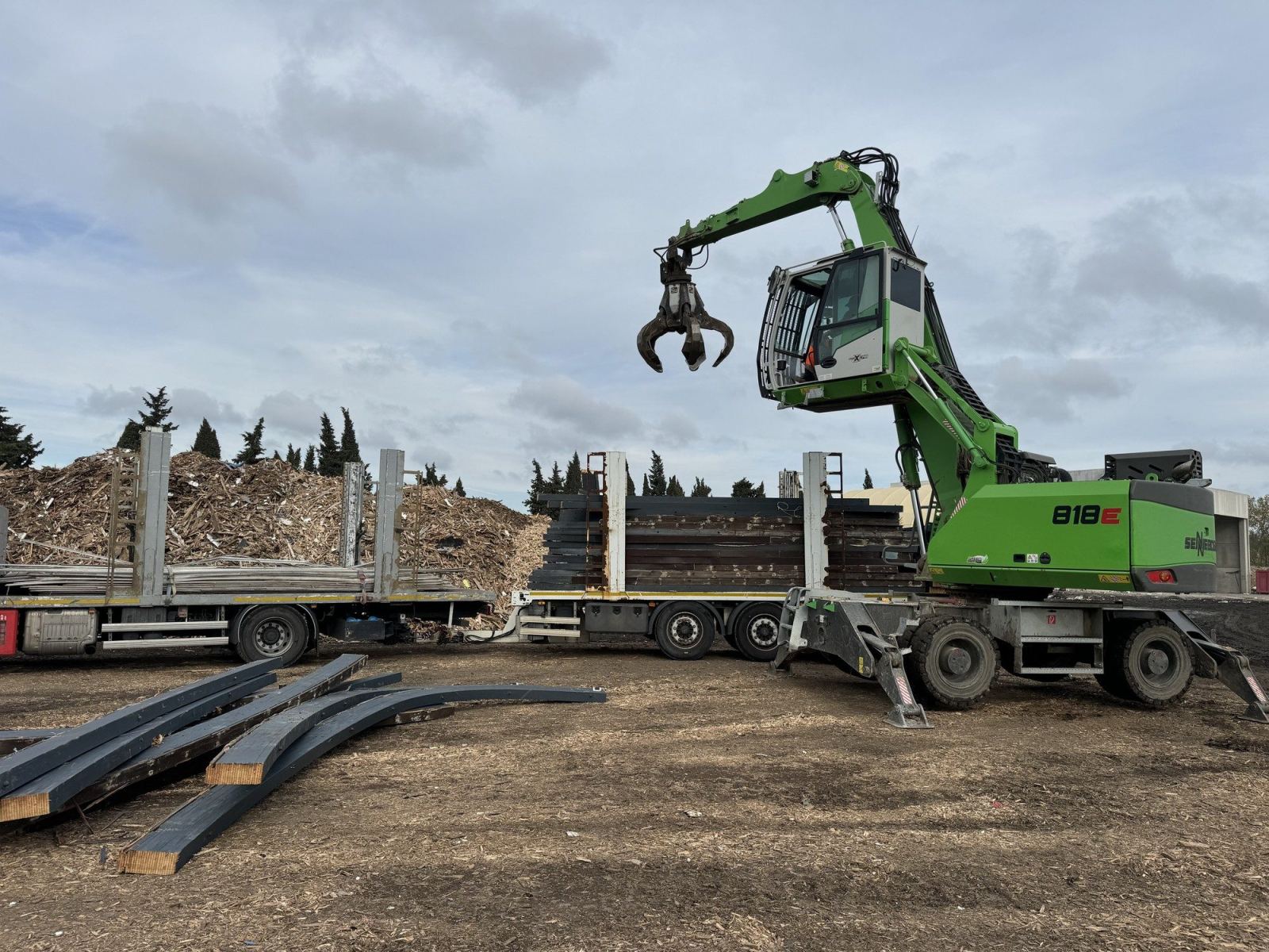 Engin de manutention à pince au-dessus d’un plateau chargé d’éléments métalliques.
