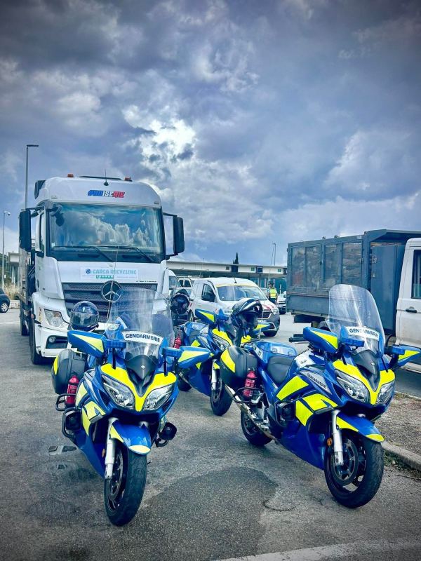 Plusieurs motos de la gendarmerie stationnées devant des poids lourds.